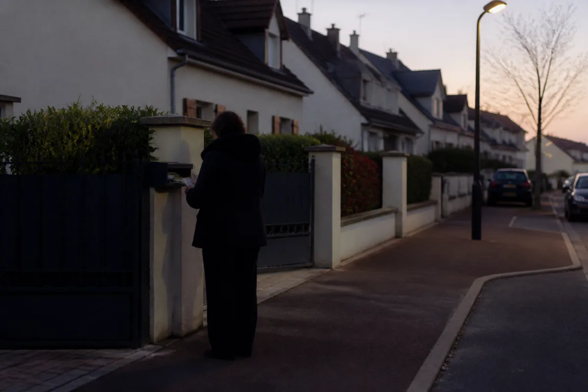 Voisin relevant le courrier d’une maison voisine et entrouvrant un volet en fin de journée